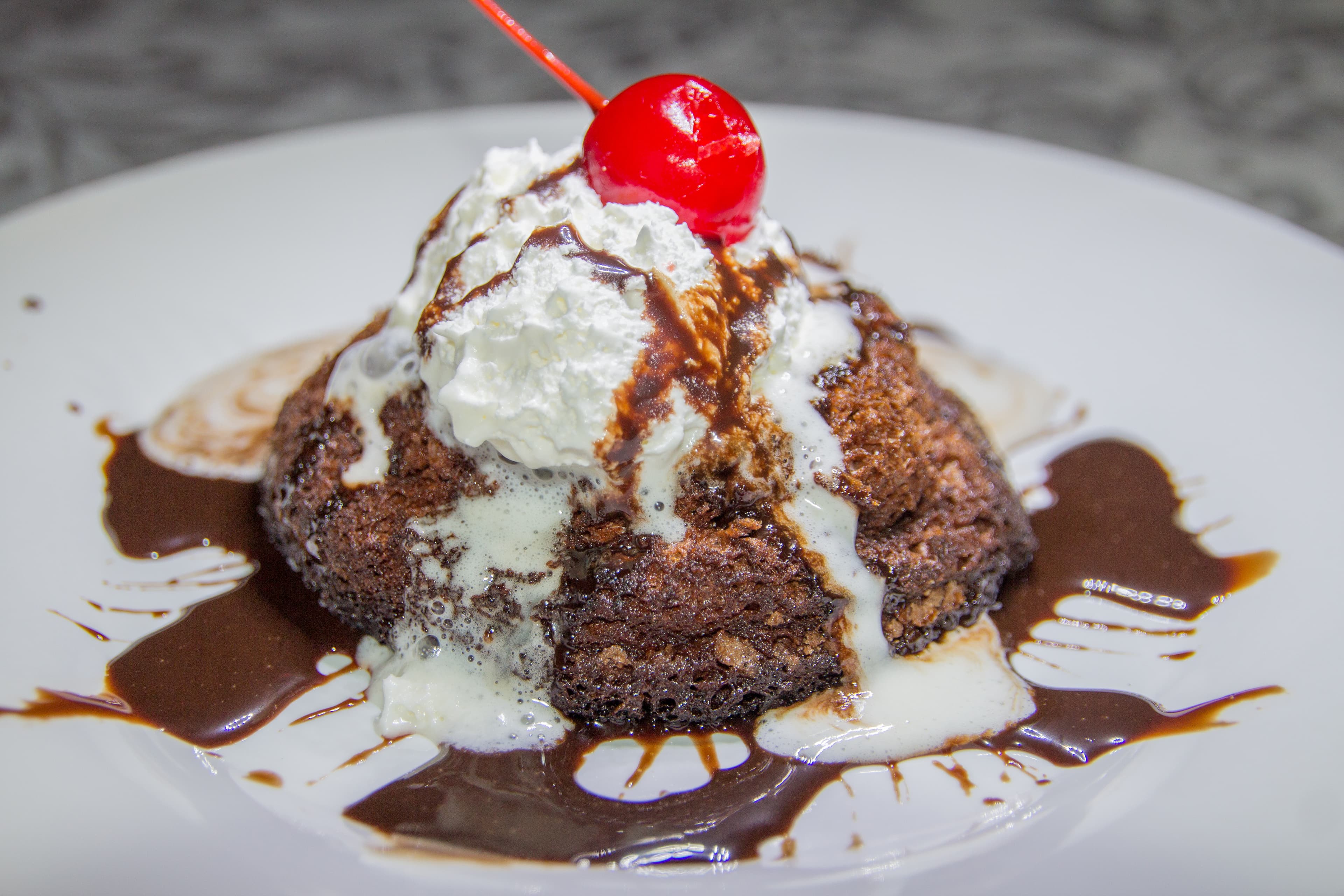 A chocolate dessert topped with whipped cream and a maraschino cherry, drizzled with chocolate sauce.