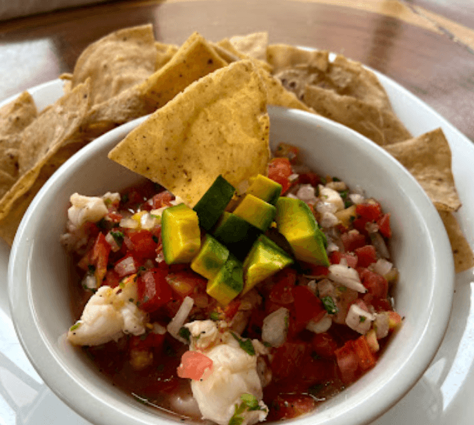 A bowl of fresh ceviche topped with avocado cubes and served with crispy tortilla chips.