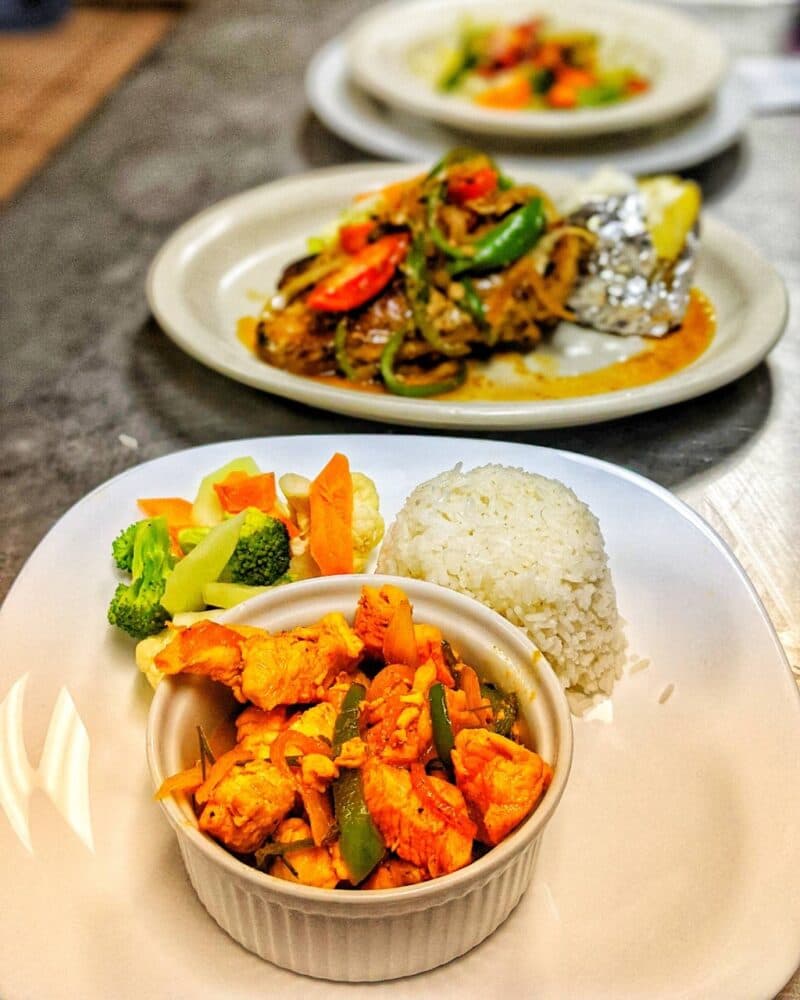 A plate featuring chicken stir-fry with vegetables, a side of steamed rice, and colorful steamed vegetables.