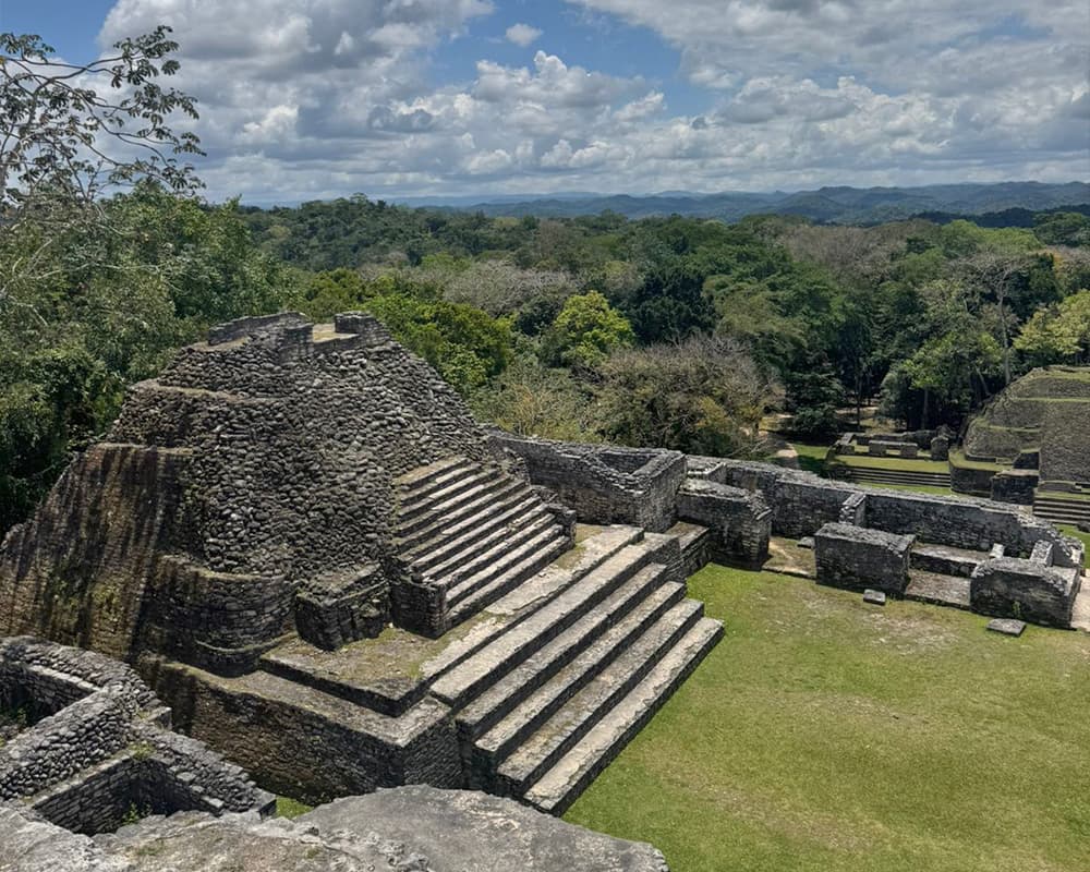 Ancient stone ruins with steps set amidst lush greenery and a cloudy sky.