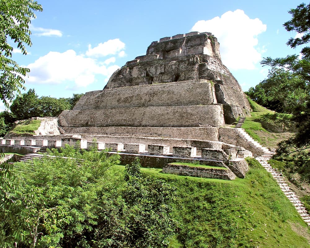 Ancient Mayan pyramid surrounded by lush greenery under a bright blue sky.